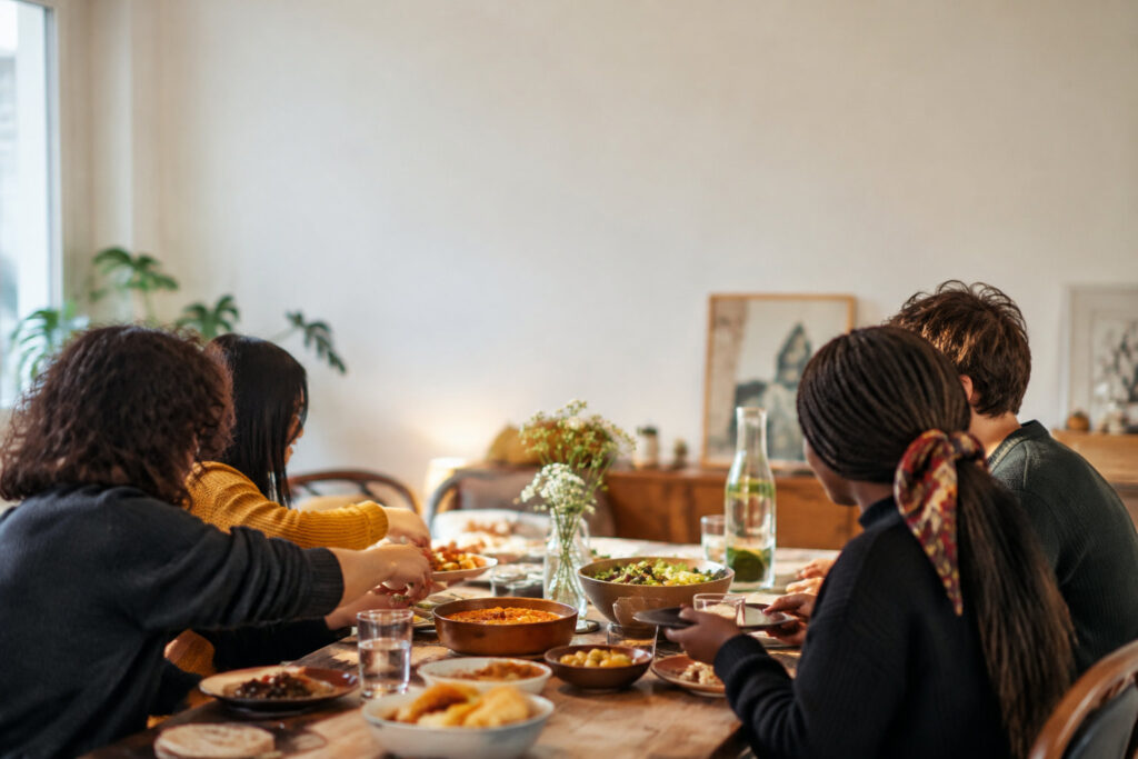 Un groupe d'étudiants internationaux partageant un repas convivial autour d'une table en bois garnie de plats variés.
