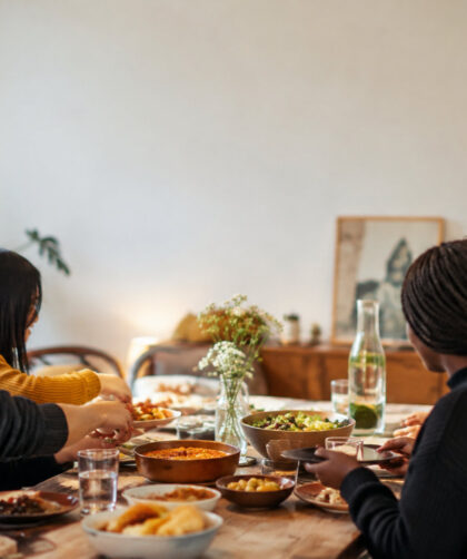 Un groupe d'étudiants internationaux partageant un repas convivial autour d'une table en bois garnie de plats variés.